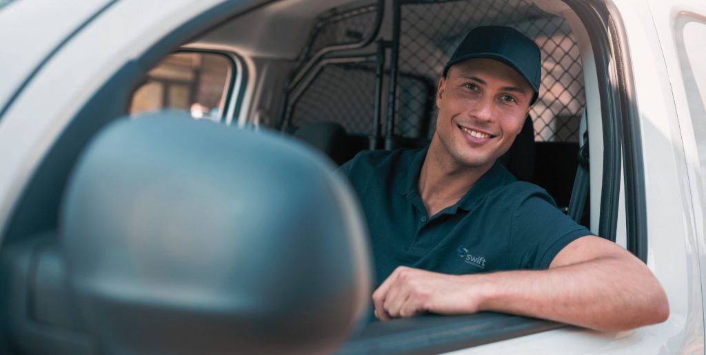 Driver in dark polo and cap sits in white vehicle, representing reliable Melbourne industrial transport services.