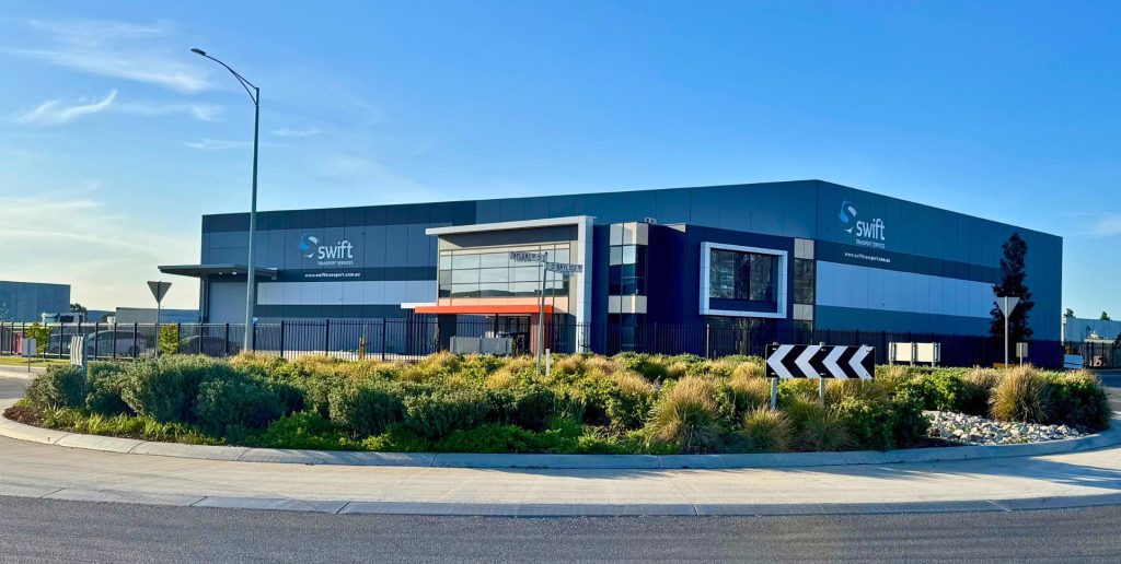 Modern industrial building with Swift signage, reliable transport fleet in Melbourne, landscaped corner, clear sky.